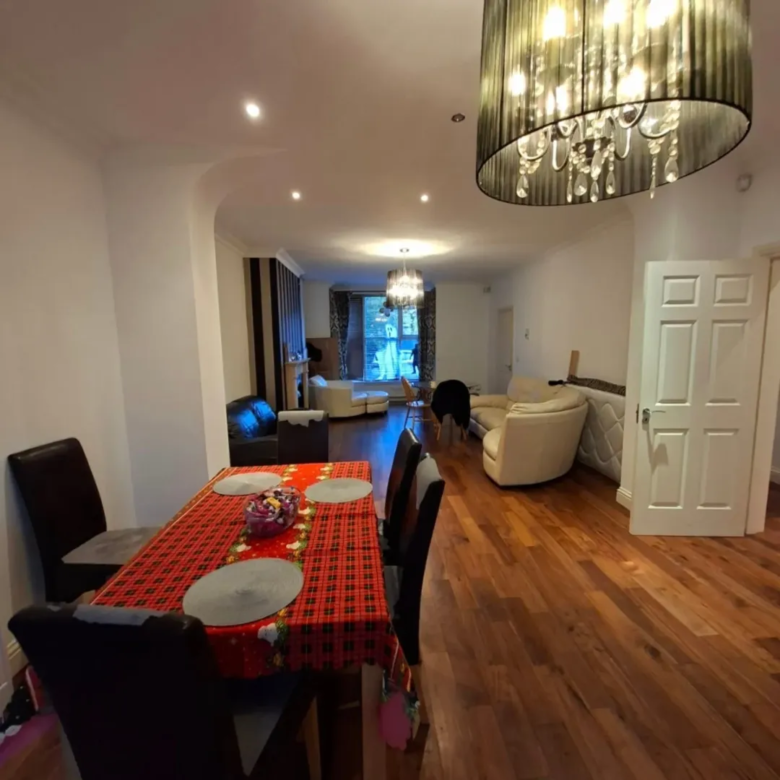 Dining room with red tablecloth and open living area. Modern chandelier.