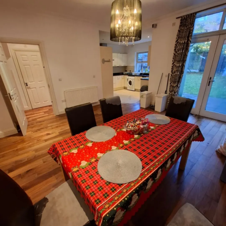 Dining room with red plaid tablecloth, chandelier, and open kitchen view.