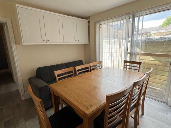 Dining room with wooden table, chairs, sofa, and overhead cabinets.
