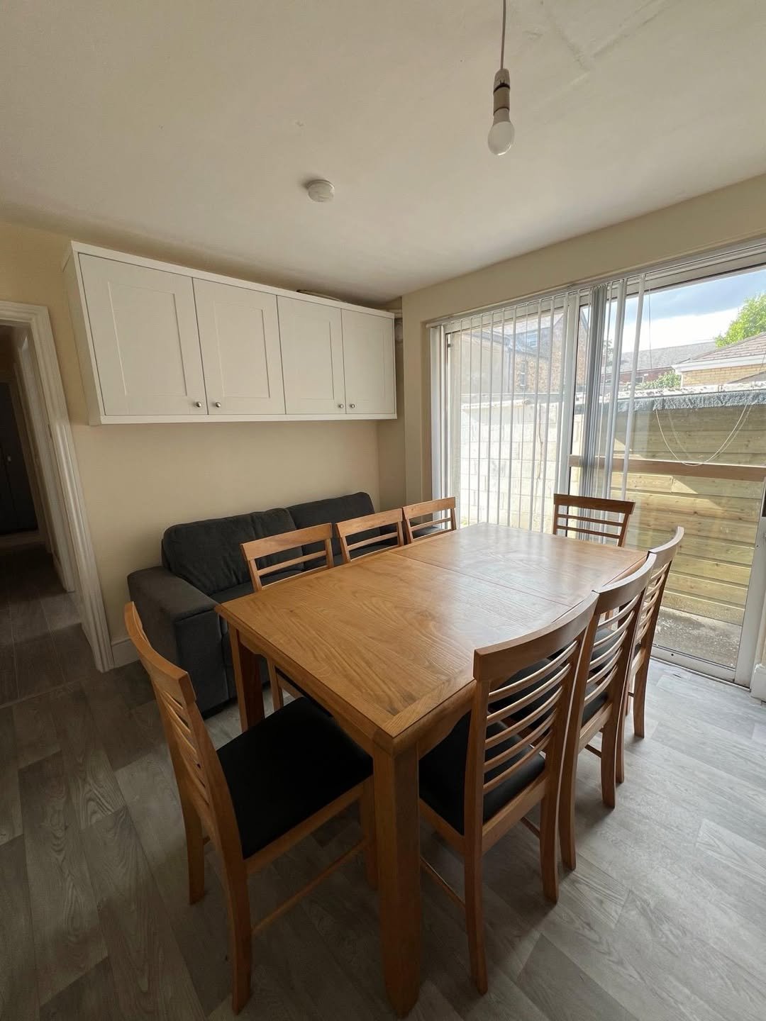 Dining room with wooden table, chairs, sofa, and overhead cabinets.