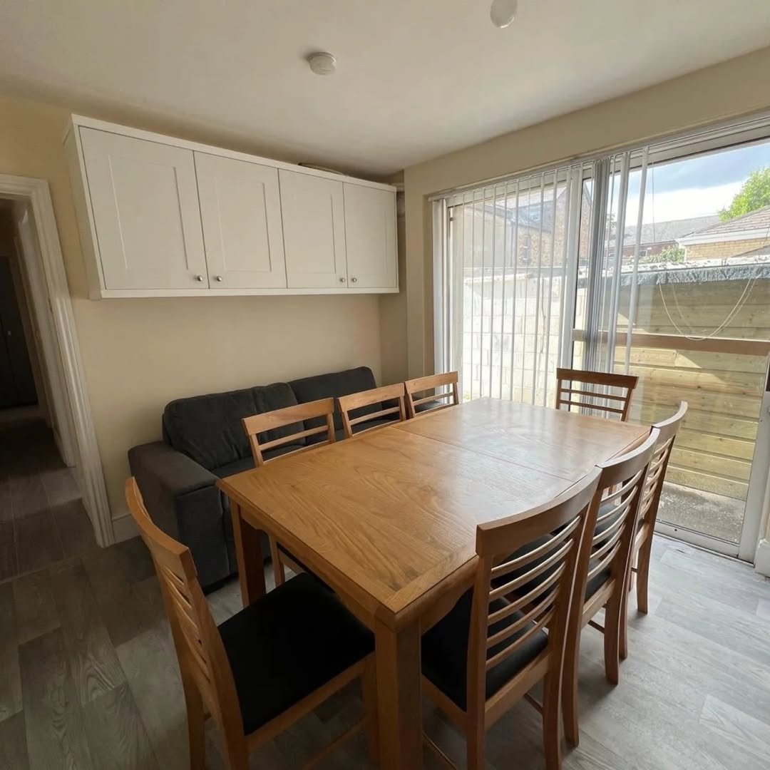 Dining room with wooden table, chairs, gray sofa, and white cabinets.