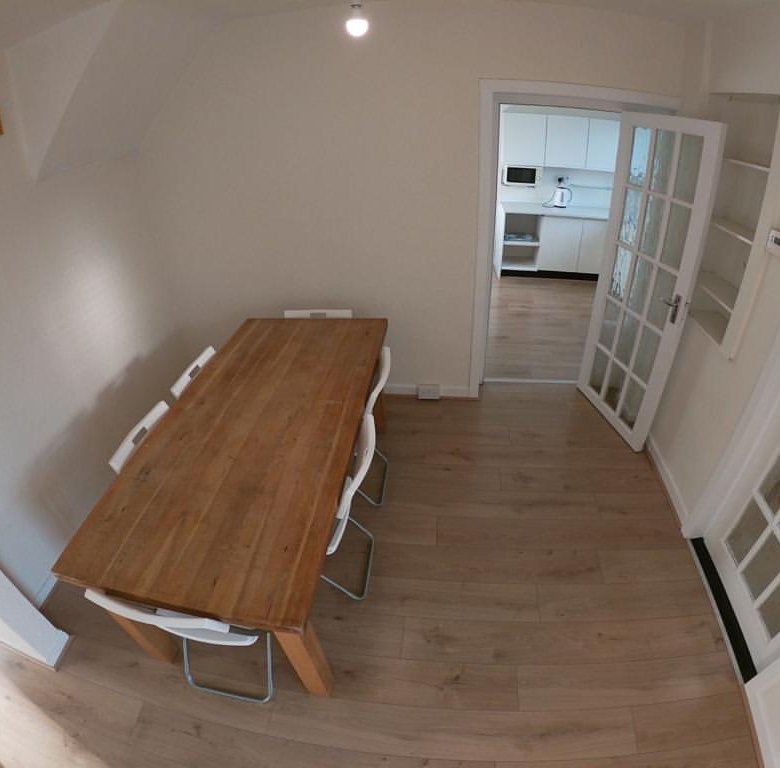 Dining room with wooden table, white chairs, and view into kitchen.