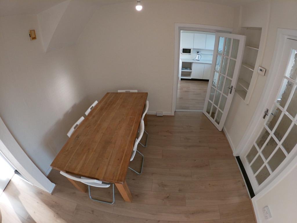 Dining room with wooden table, white chairs, and view into kitchen.