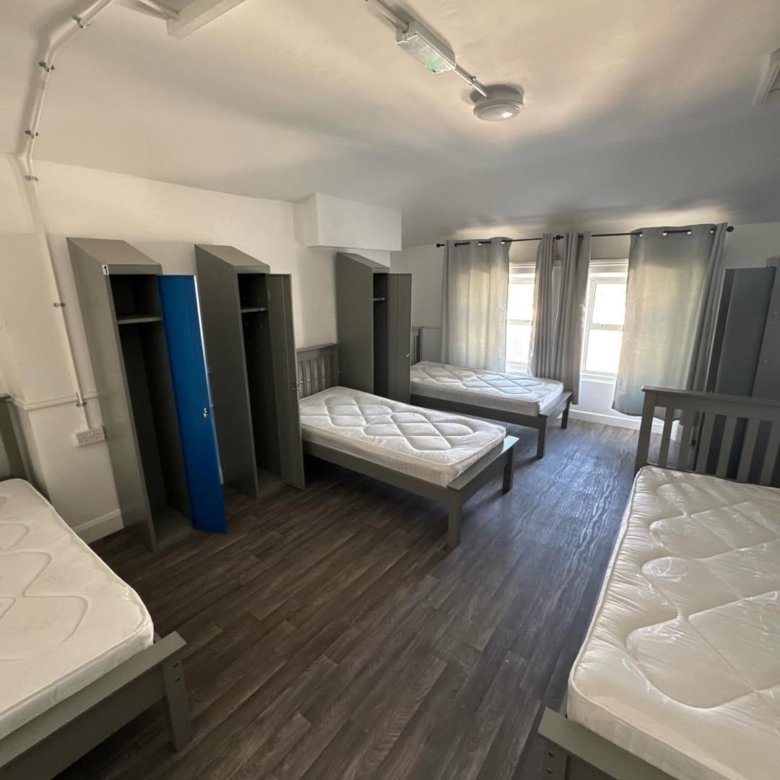 Dorm room with four beds, lockers, and windows. Simple, functional interior design.