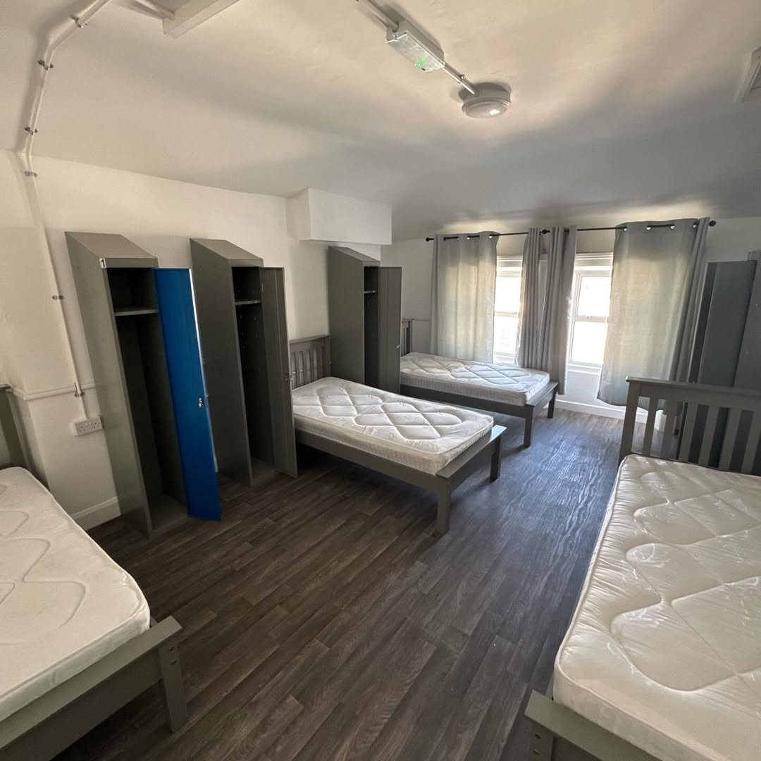 Dorm room with four beds, lockers, and windows. Simple, functional interior design.