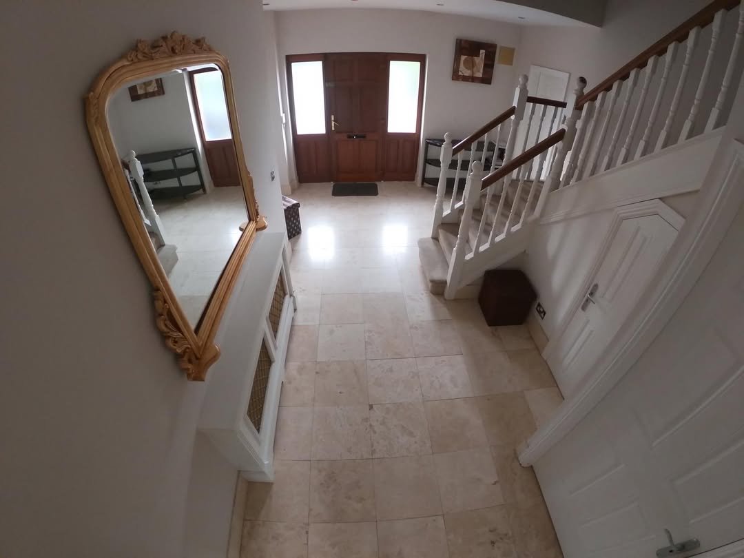 Foyer featuring tile flooring, wooden door, staircase, mirror, and white console table.