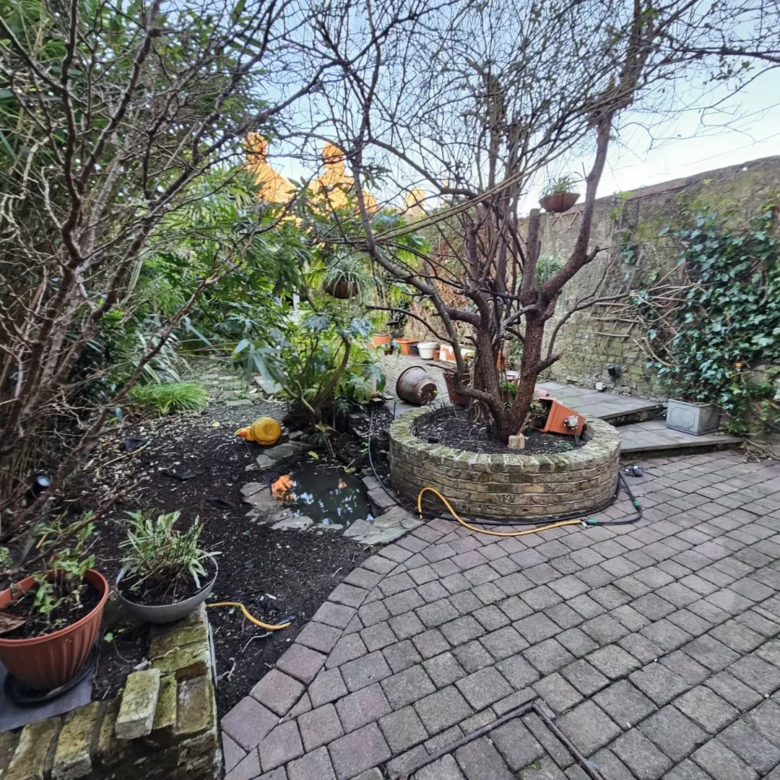 Garden with brick patio, small pond, and bare tree encircled by brickwork.