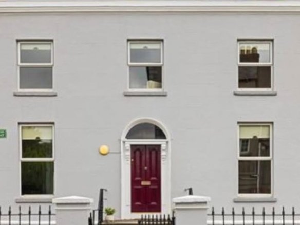 Gray Georgian house with symmetrical windows and a maroon front door under a blue sky.