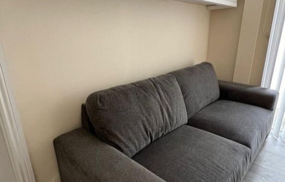 Gray sofa against a neutral wall with white door and window blinds.
