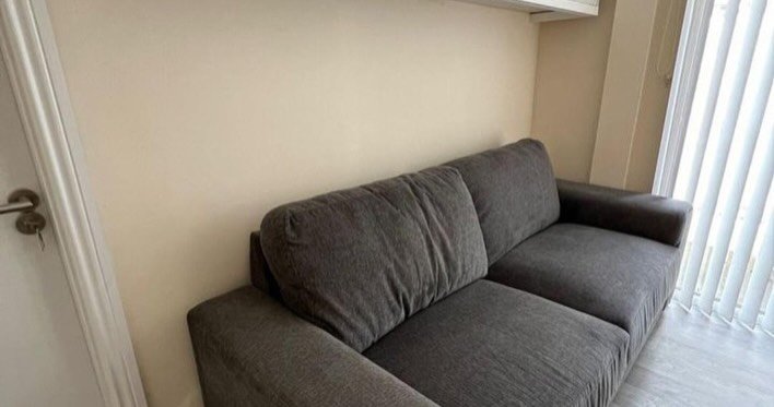 Gray sofa against a neutral wall with white door and window blinds.