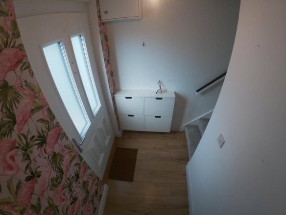 Hallway with flamingo wallpaper, white door, shoe storage, and wooden floor.