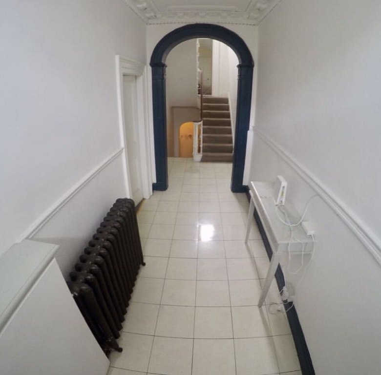 Hallway with radiator, table, and archway leading to stairs in a bright, tiled interior space.