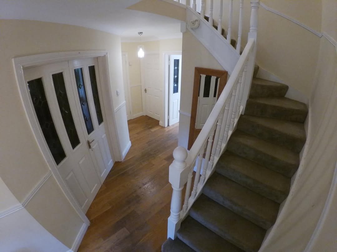 Hallway with staircase, white paneled doors, and wood flooring in a home interior.