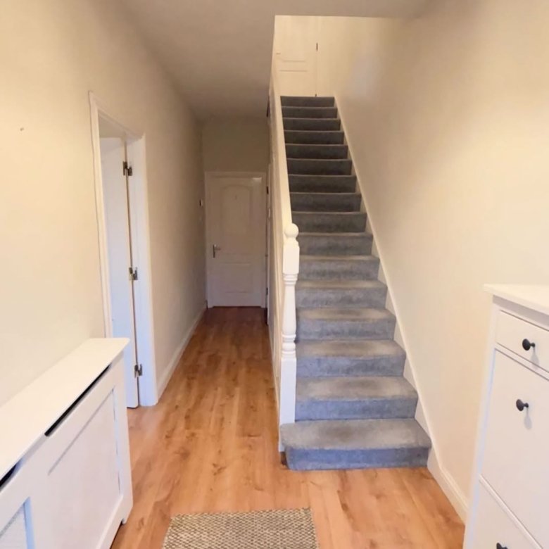 Hallway with stairs, wooden floors, and white trim. Neutral interior design.