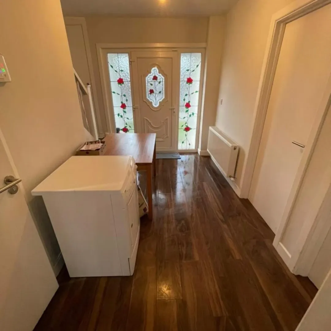 Hallway with wood floor, stained glass door, white cabinet and table.