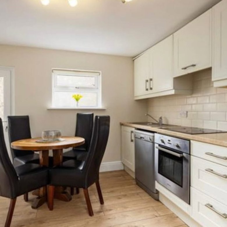 Kitchen with dining table, cream cabinets, stainless steel appliances, and wood-look flooring.