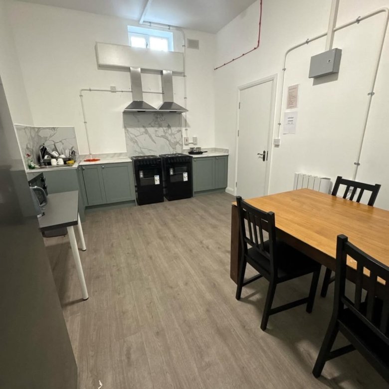 Kitchen with light gray cabinets, marble backsplash, black stoves, a wooden table, and black chairs.