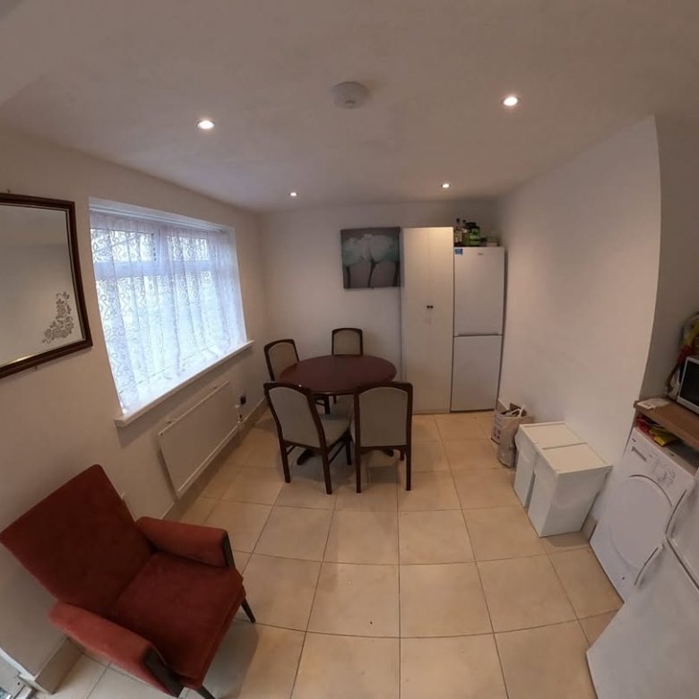 Cozy kitchen with red armchair, dining table, and white appliances under natural light.