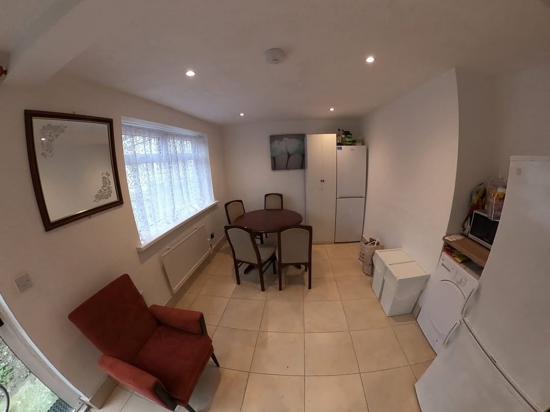 Cozy kitchen with red armchair, dining table, and white appliances under natural light.