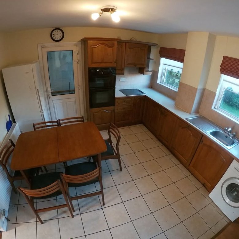 Cozy kitchen with wooden cabinets, dining table, white appliances, and tile flooring. Natural light from windows.