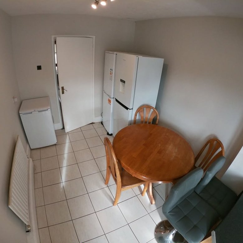 Kitchen interior with round wooden table, chairs, refrigerator, and white door. Tiled floor and radiator.