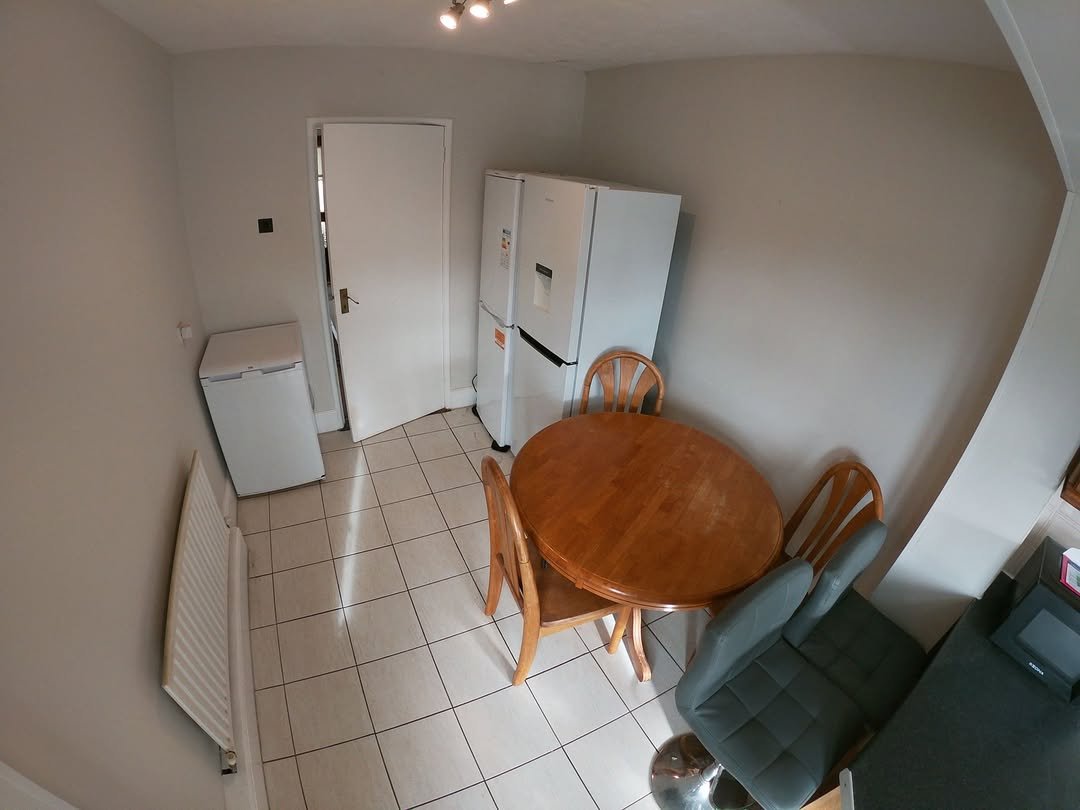 Kitchen interior with round wooden table, chairs, refrigerator, and white door. Tiled floor and radiator.