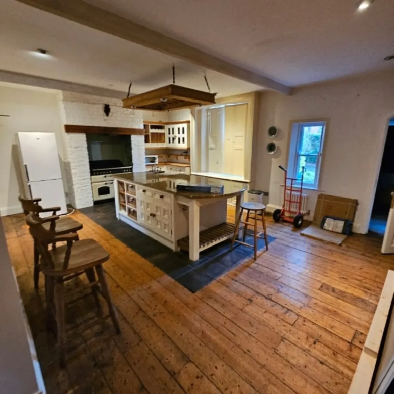 Spacious kitchen with island, wooden floors, brick fireplace, and white appliances.