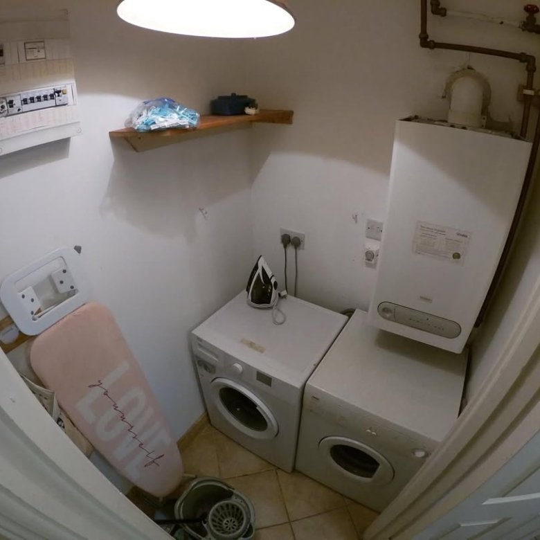 Laundry room with washing machines, ironing board, boiler, and electrical panel.