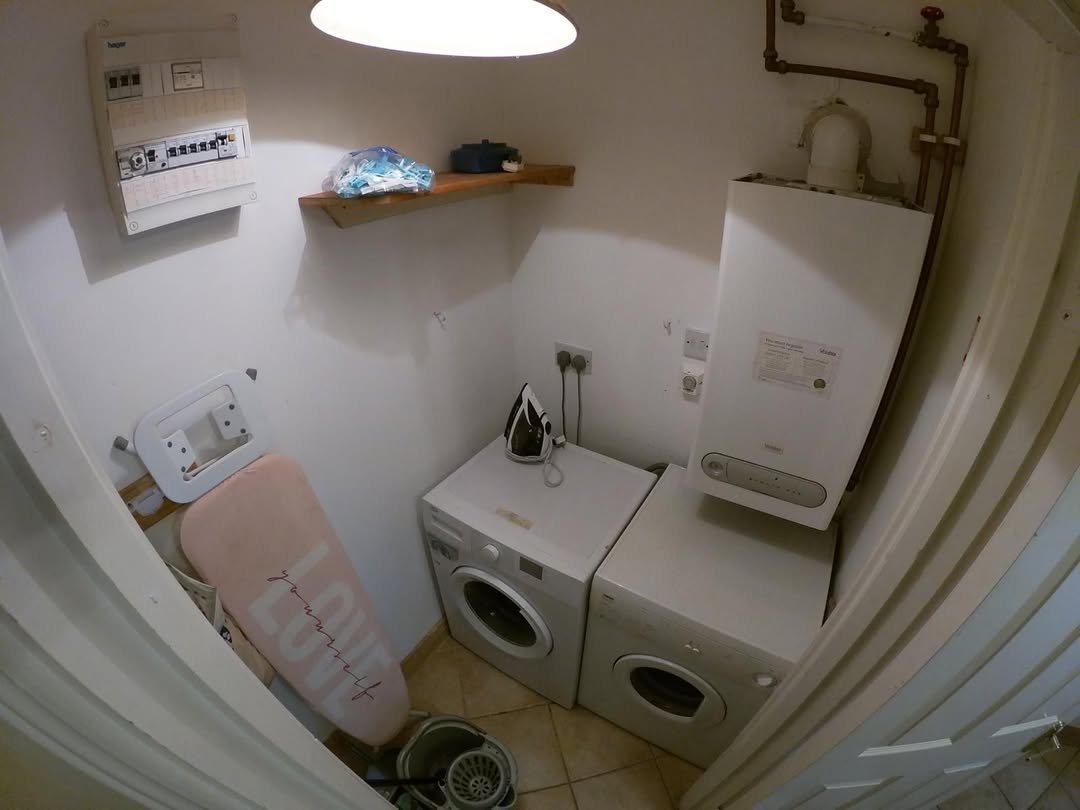 Laundry room with washing machines, ironing board, boiler, and electrical panel.
