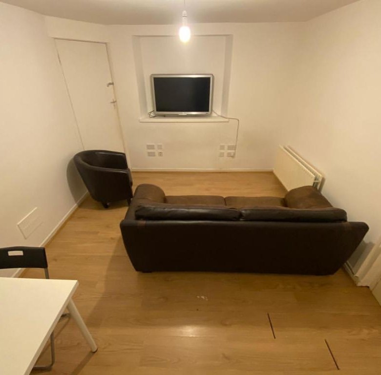Cozy living room with brown sofa, chair, TV, and white walls.
