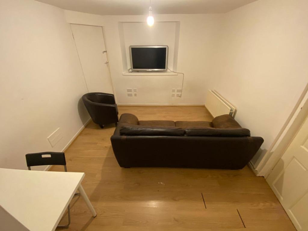 Cozy living room with brown sofa, chair, TV, and white walls.
