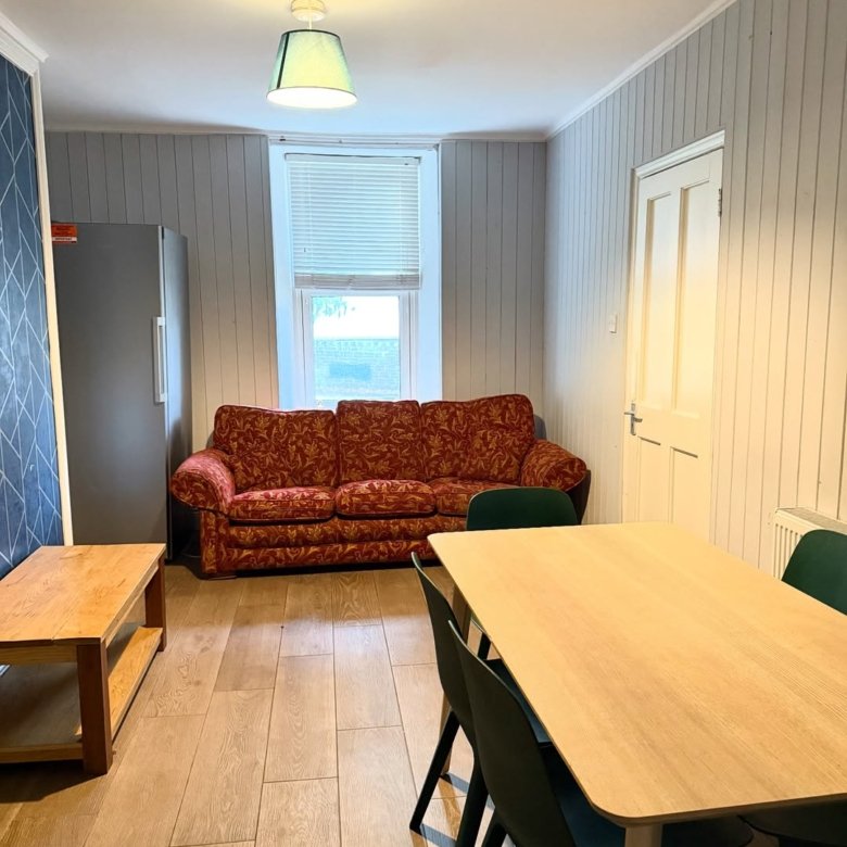 Living room with red sofa, dining table, wood floors, and paneled walls.