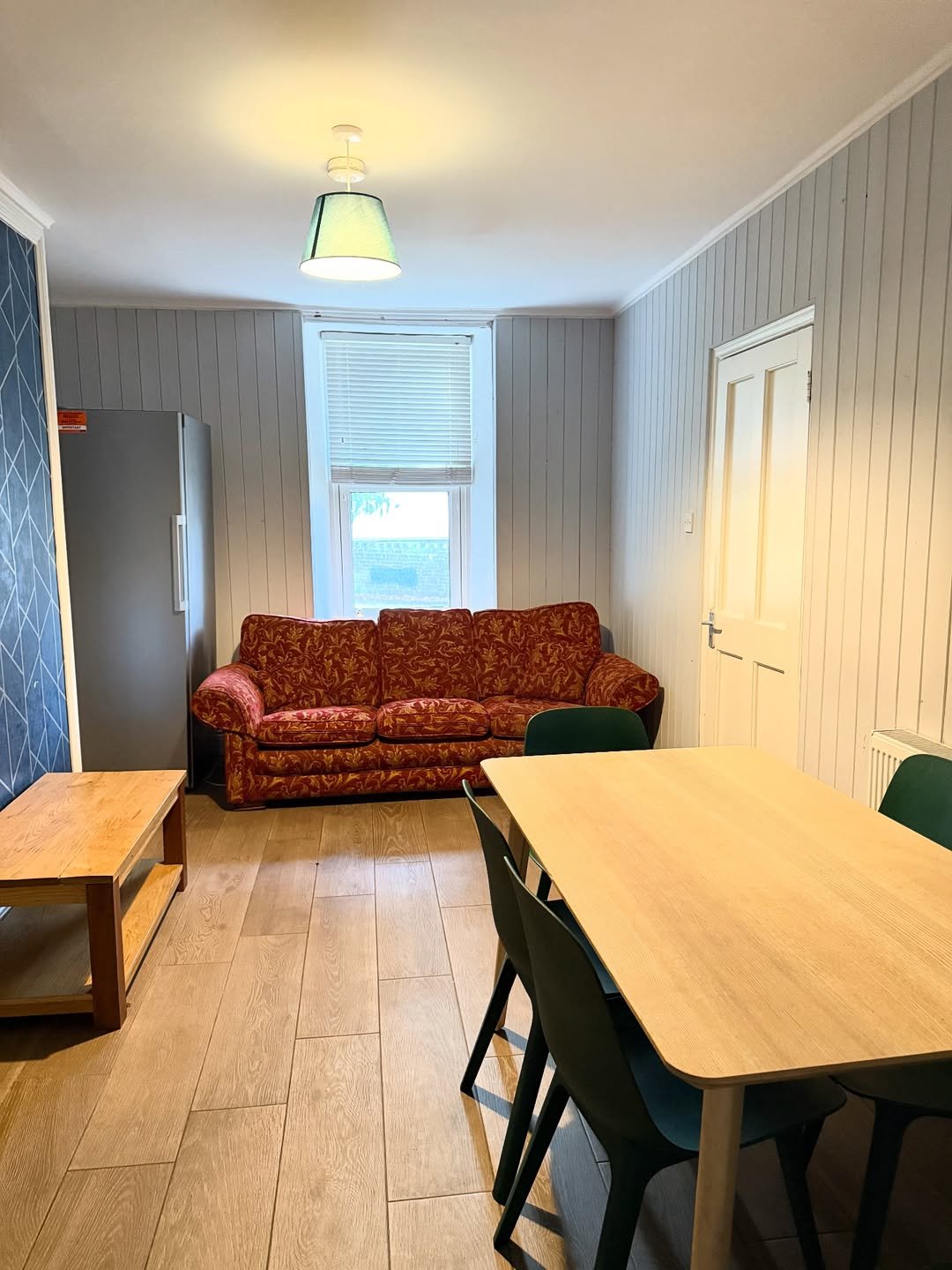 Living room with red sofa, dining table, wood floors, and paneled walls.