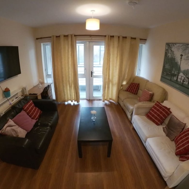Cozy living room with sofas, black coffee table, TV, and artwork in a well-lit apartment.