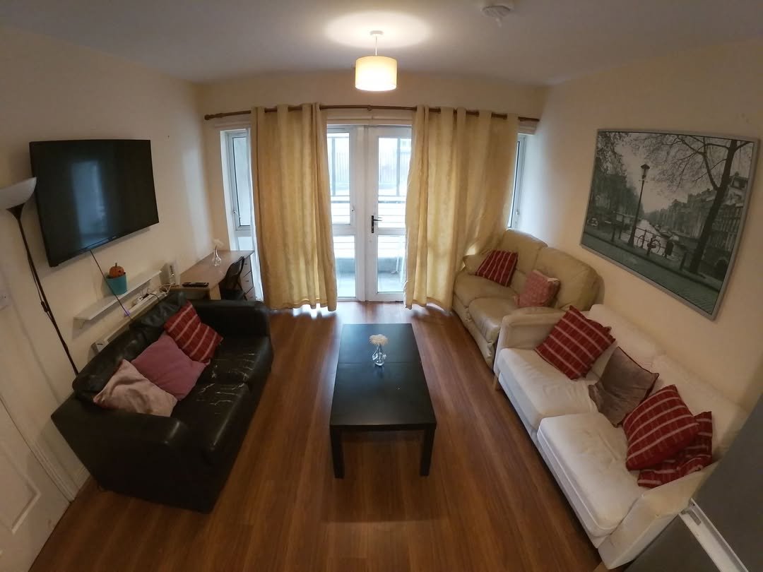 Cozy living room with sofas, black coffee table, TV, and artwork in a well-lit apartment.