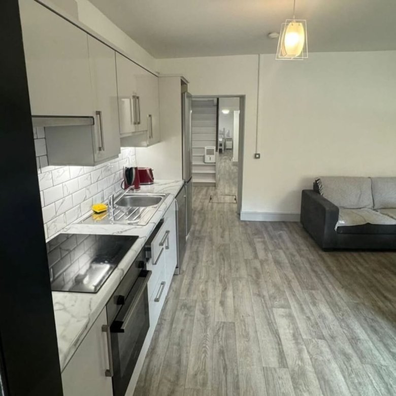 Modern apartment kitchen and living area with wood floors and white cabinets.