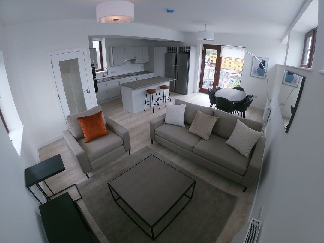 Modern apartment living room with open kitchen, gray sofa and armchair, and dining area.