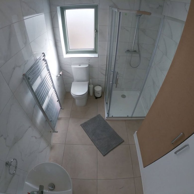 Modern bathroom with toilet, shower, sink, and heated towel rack. Neutral color scheme.