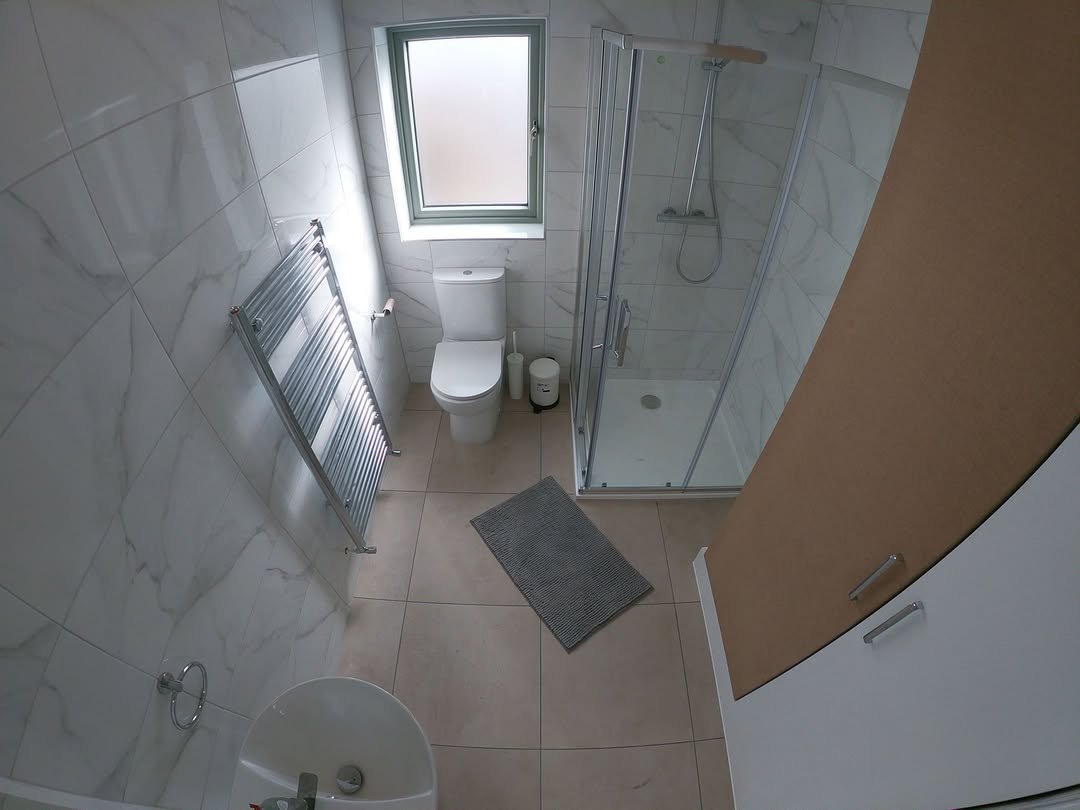 Modern bathroom with toilet, shower, heated towel rack, and small sink.