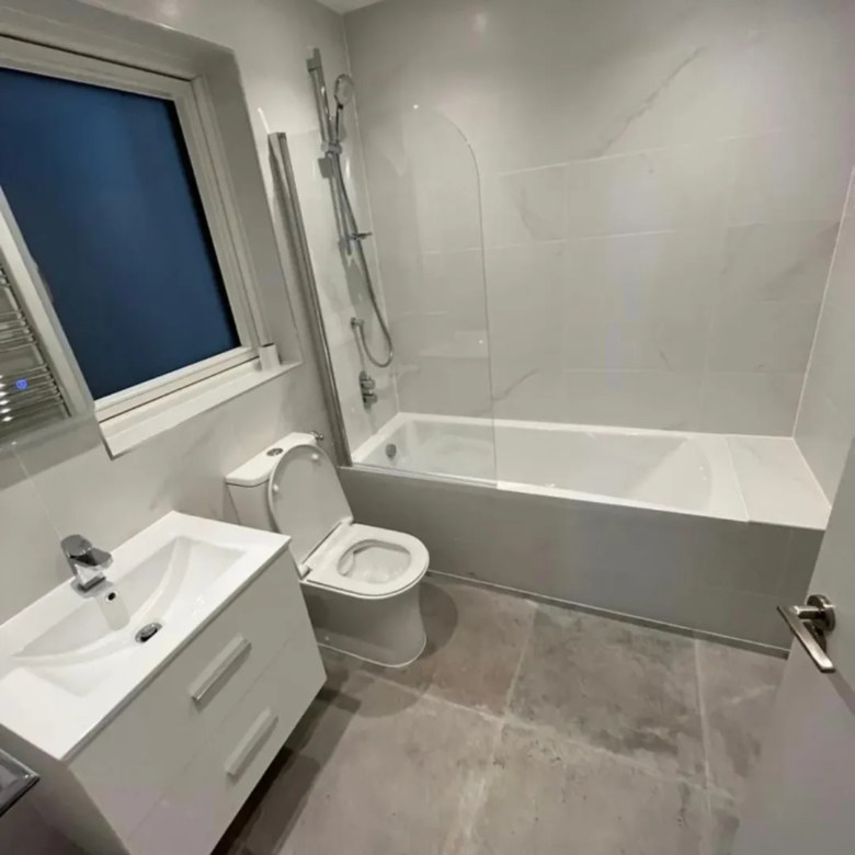 Modern bathroom with white vanity, toilet, and bathtub with glass shower screen.