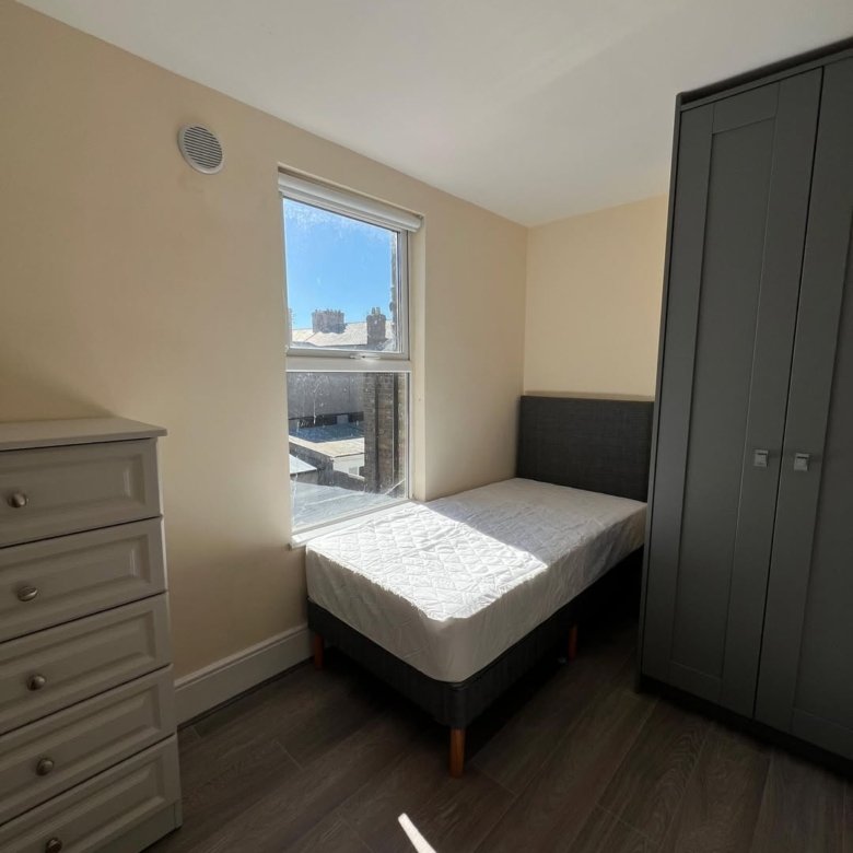 Bedroom with single bed, gray wardrobe, chest of drawers, and window with rooftop view. Modern interior design.