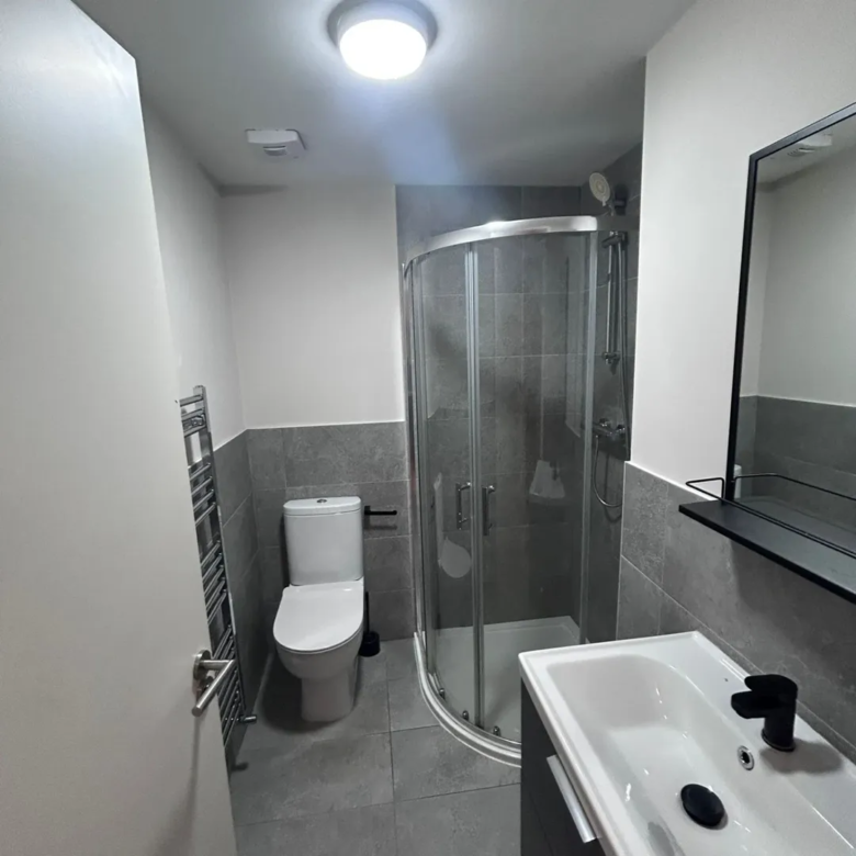 Modern gray bathroom with shower, toilet, sink, and towel rack.