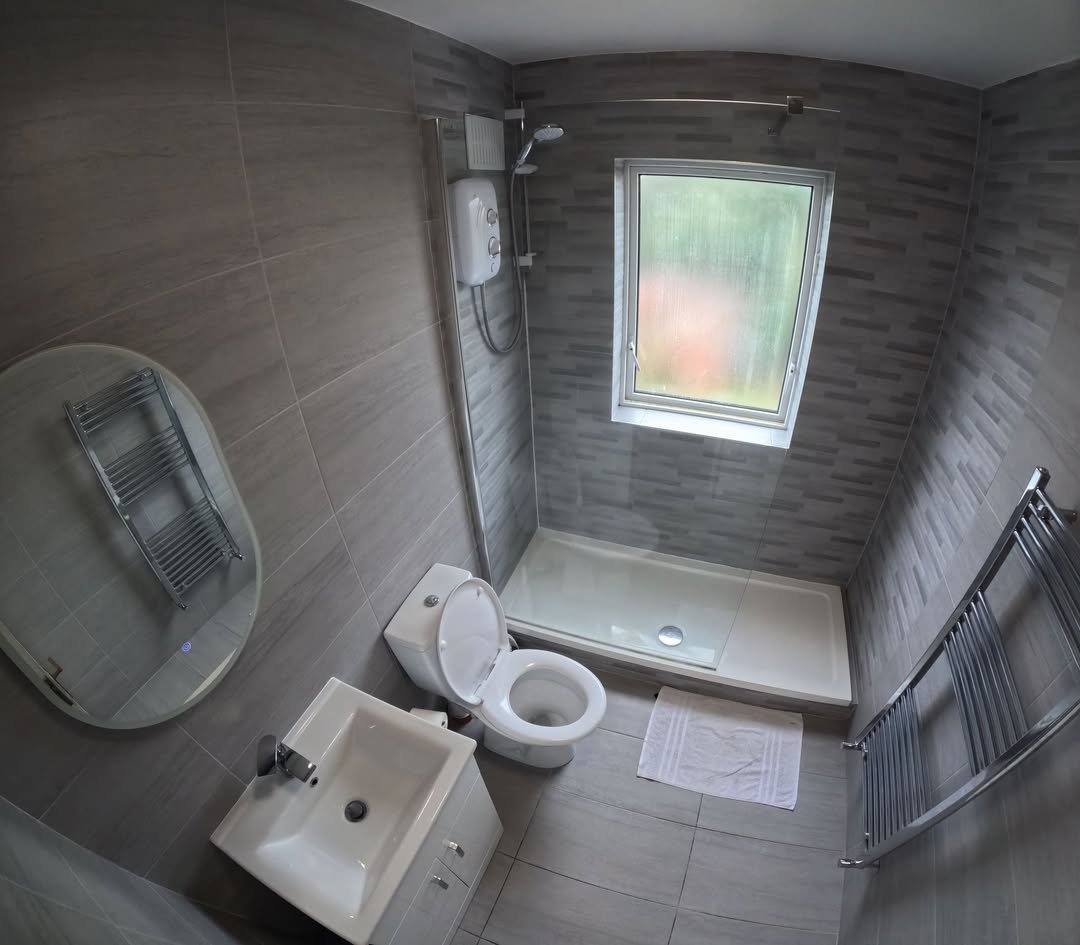 Modern gray bathroom with toilet, sink, shower, and heated towel rack.