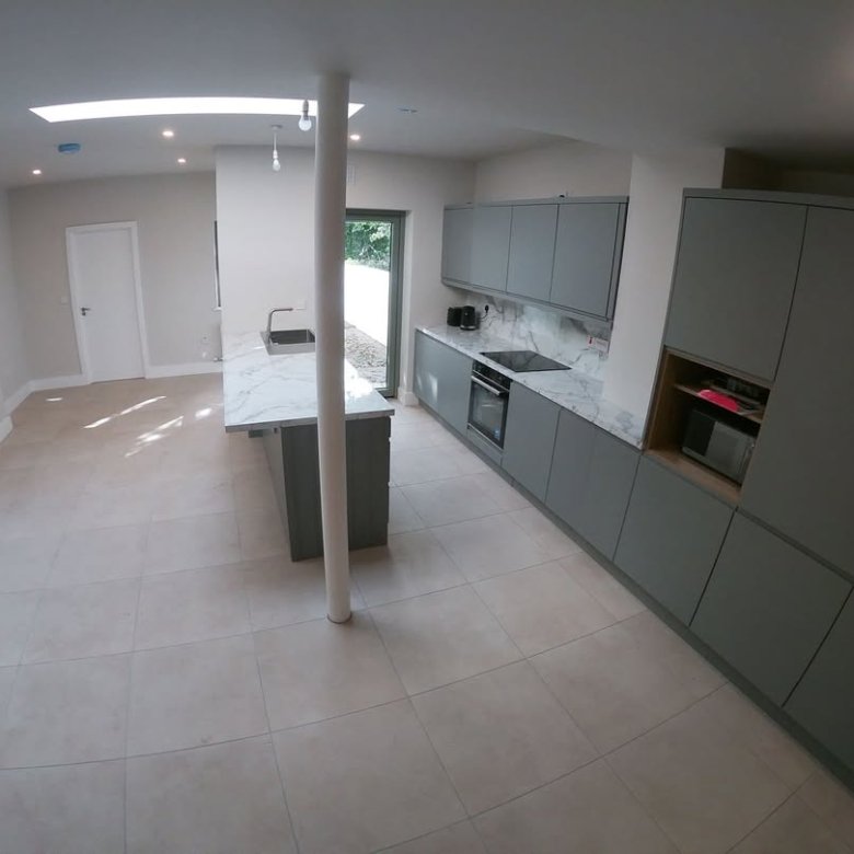 Modern gray kitchen with island, integrated appliances, and tile floor.