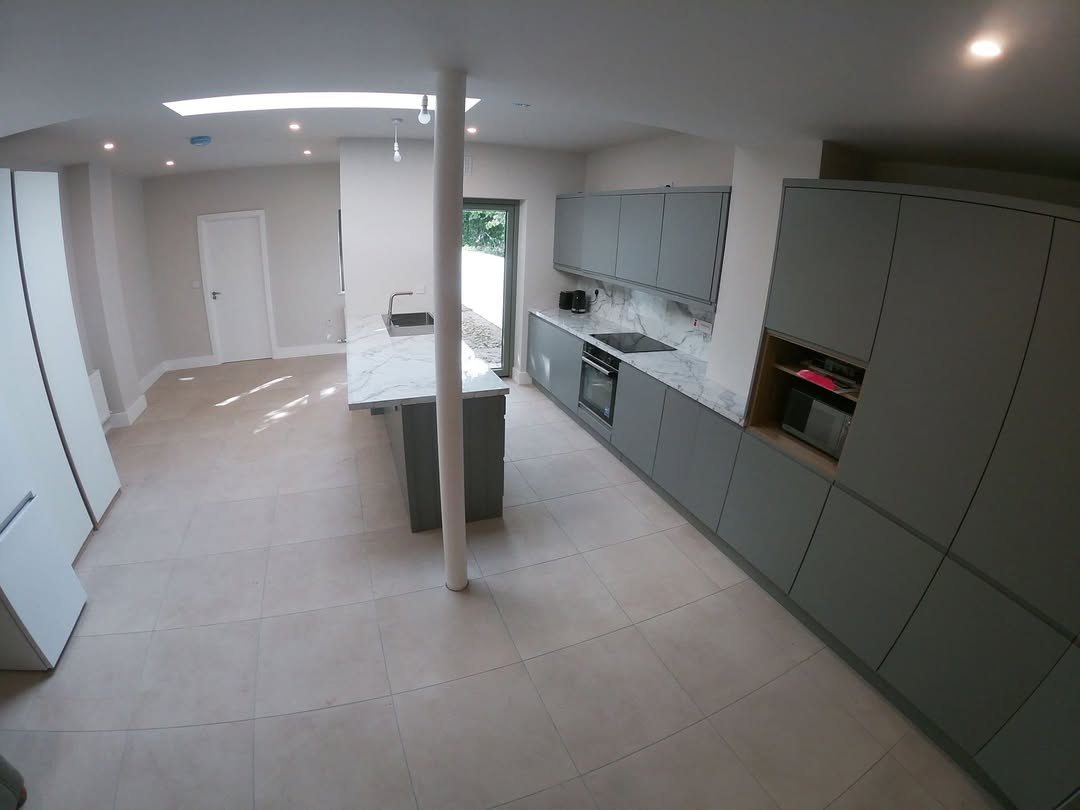 Modern gray kitchen with island, integrated appliances, and tile floor.