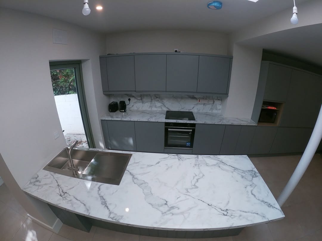 Modern gray kitchen with marble countertop island and stainless steel sink.