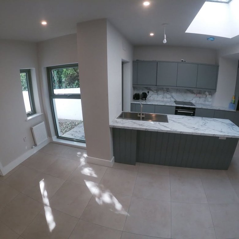 Modern kitchen with gray cabinets, marble island, and skylight. Bright, open space with tile flooring.