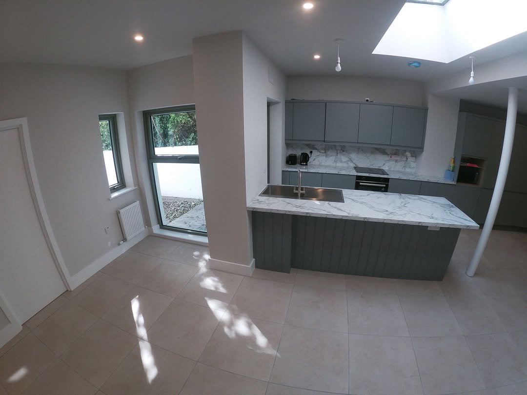 Modern kitchen with gray cabinets, marble island, and skylight. Bright, open space with tile flooring.