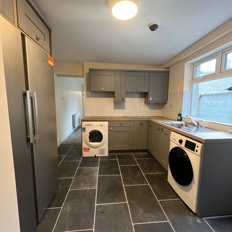 Modern gray kitchen with slate flooring, stainless steel fridge, and white washer/dryer units.