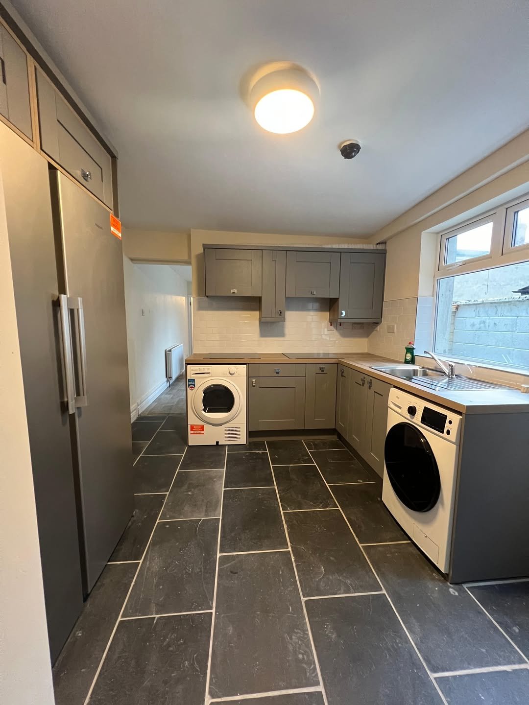 Modern gray kitchen with slate flooring, stainless steel fridge, and white washer/dryer units.